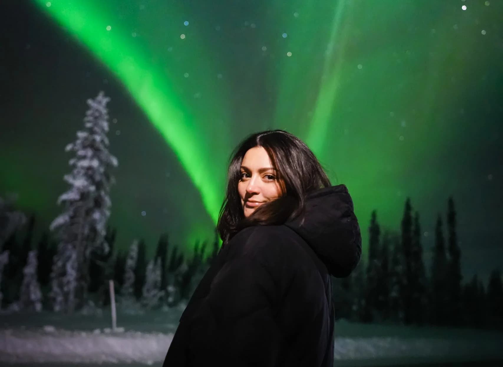 Guest smiling under a green aurora in a snowy forest near Rovaniemi