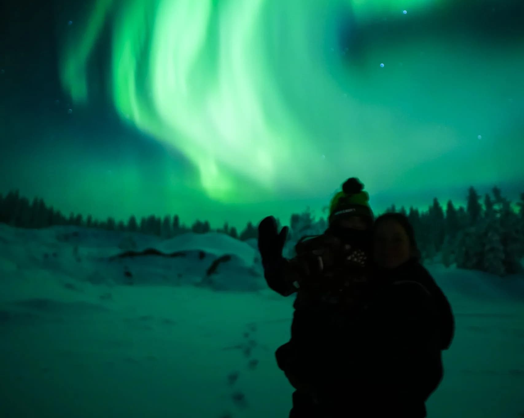 Guests waving under swirling Northern Lights on a snowy hilltop