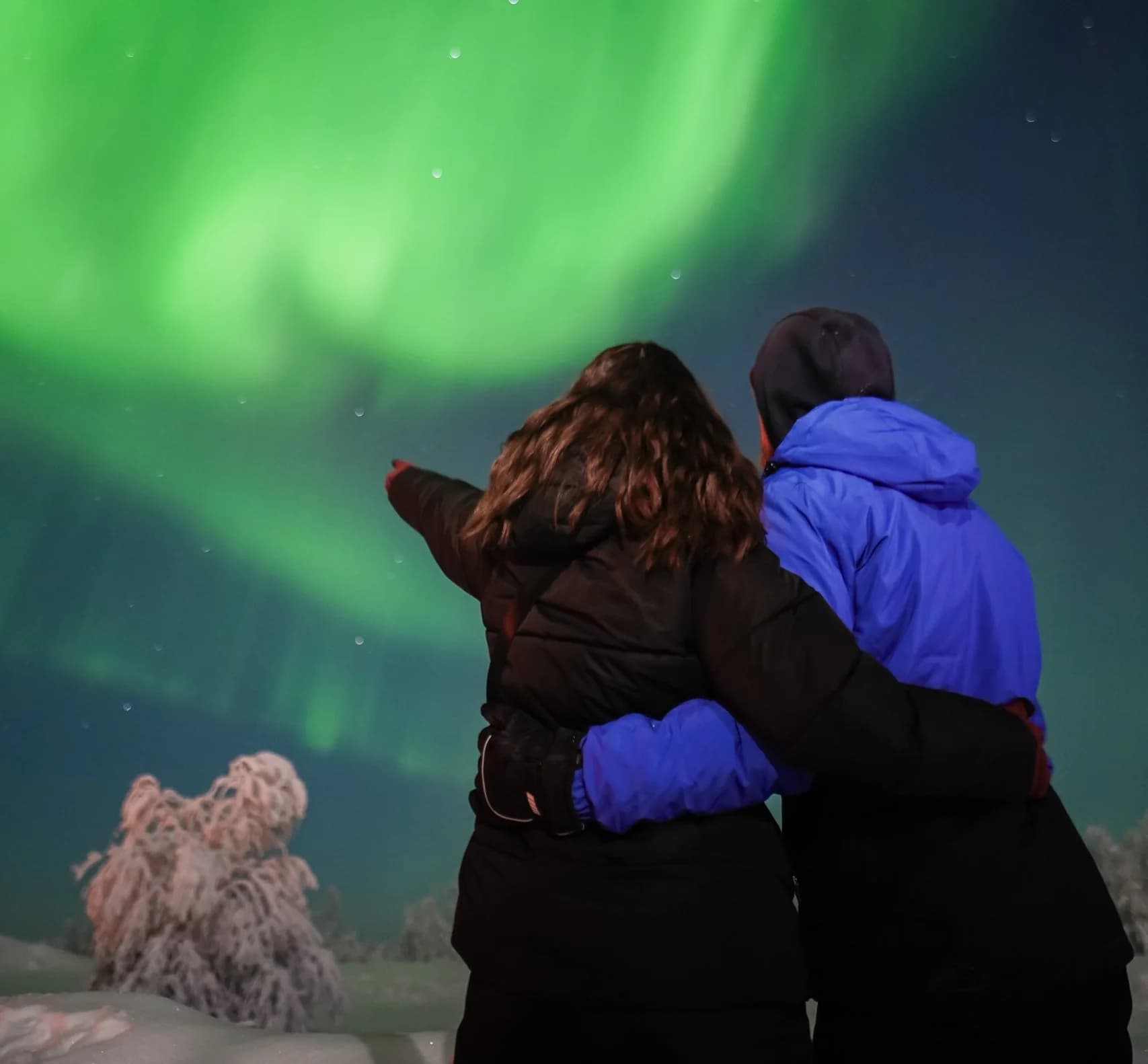Two guests pointing at bright green Northern Lights on a Book Lapland aurora tour